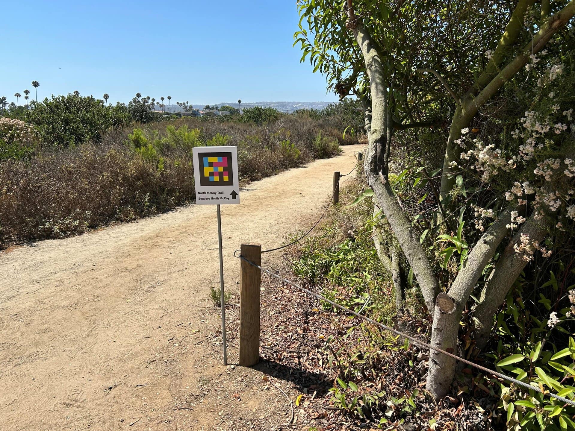 A sign near a Toyon bush has a Navilens code and an arrow pointing toward North McCoy Trail.