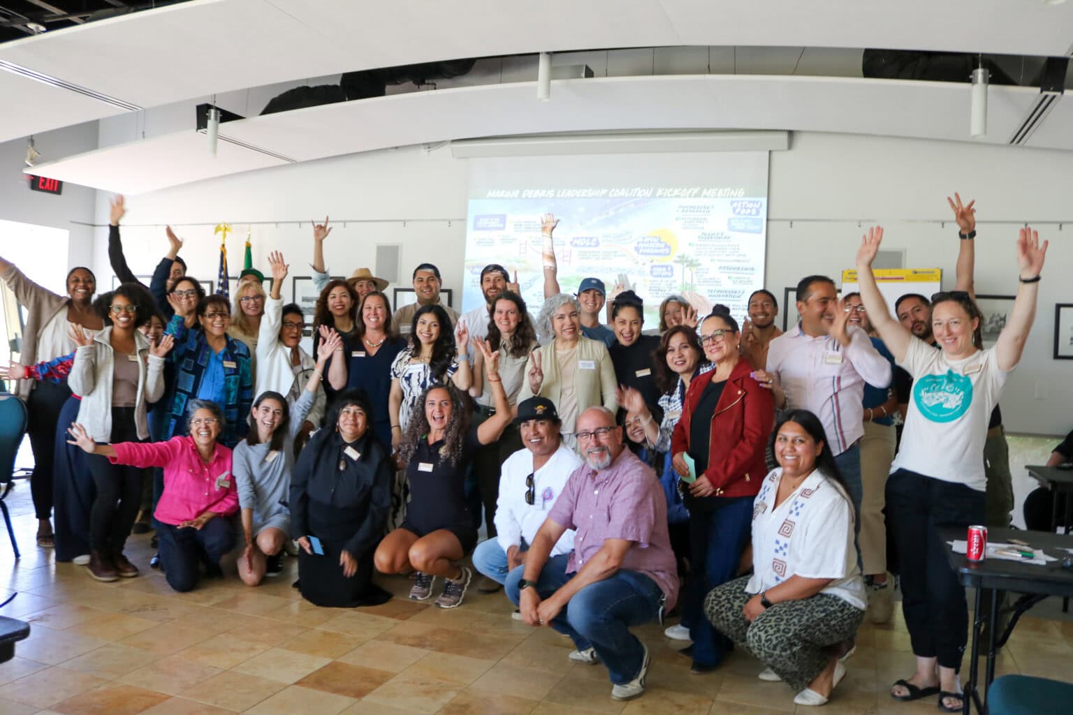 Diverse group of people celebrating at Coastal Training event in a conference room.